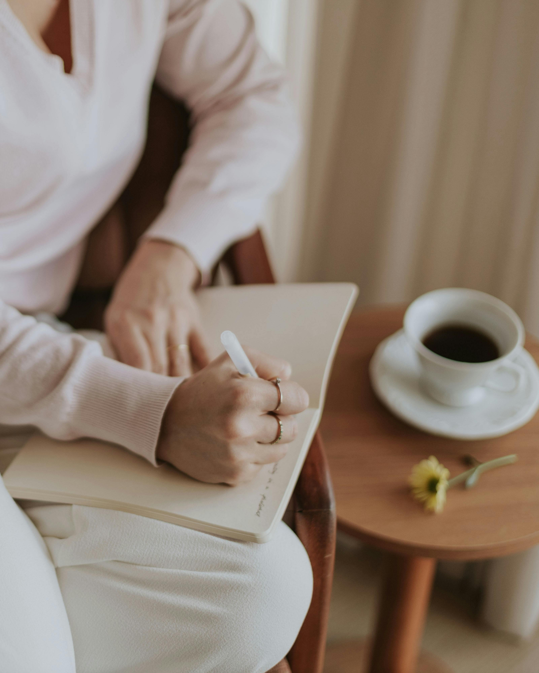 A woman writing in a journal beside a cup of coffee