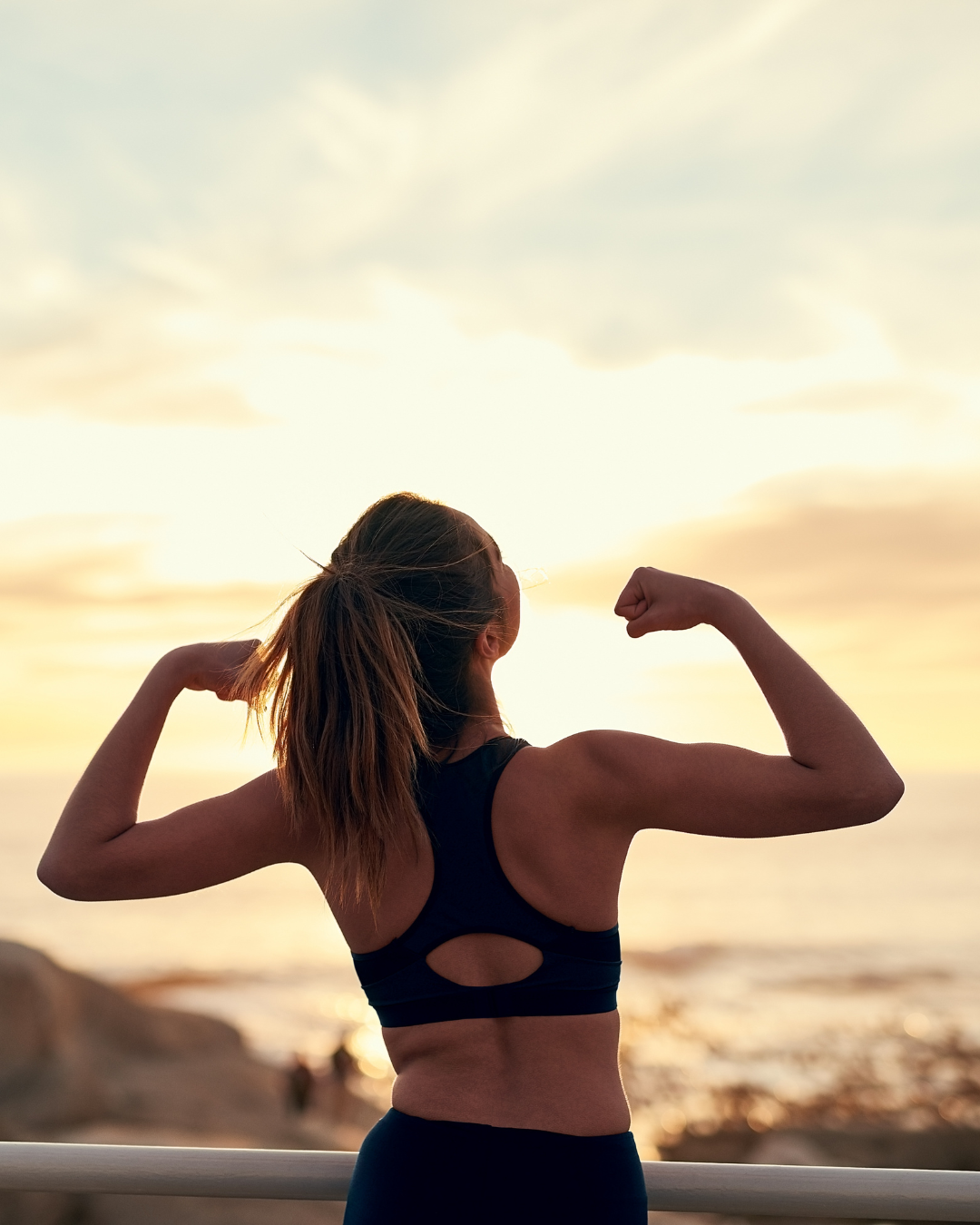 A woman flexing at sunset, seen from behind